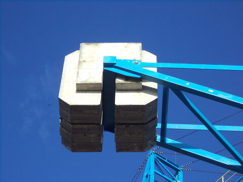 A close-up view of concrete counterweights on a blue crane against a clear sky, representing heavy lifting equipment and construction engineering.