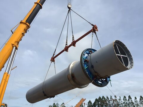 A crane hoisting a large metal cylinder in a construction site, demonstrating heavy lifting, industrial machinery, and precision engineering under a cloudy sky.