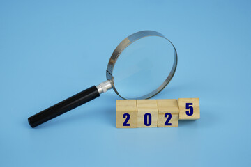 Economic forecast for year 2025. Magnifying glass and wooden cubes with numbers 2025 on blue...
