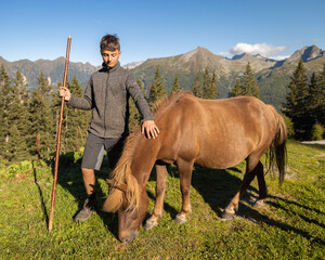 Young man interacts with a horse in a mountainous landscape during a sunny day