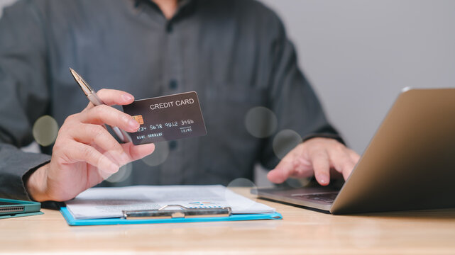 A person holds a credit card while working on a laptop, showcasing the integration of modern finance management and online shopping or banking, highlighting convenience and accessibility