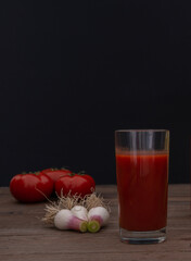Glass of tomato juice with fresh vegetables on wooden table over black background
