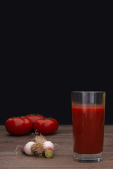 Glass of tomato juice with fresh vegetables on wooden table over black background