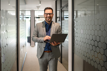 Successful young businessman in eyeglasses working on his computer while walking in office corridor