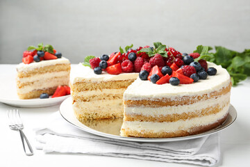 Tasty sponge cake with fresh berries and mint served on white table
