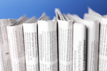 Many newspapers in different languages on blue background, closeup