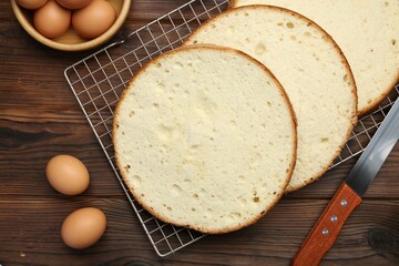 Delicious cut sponge cake, knife and ingredients on wooden table, flat lay