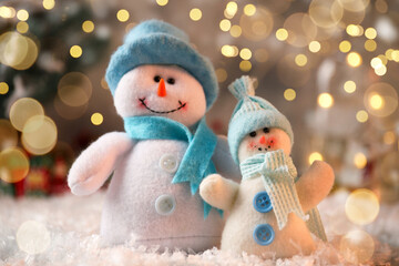 Cute snowmen against blurred Christmas lights, closeup. Bokeh effect