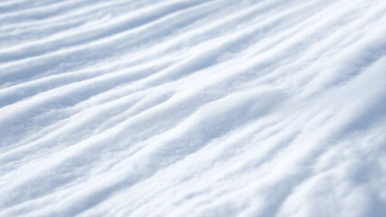 lose-up of snow-covered ground, the texture of fresh white snow, visible ripples and contours.