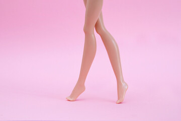 Plastic dolls legs standing on a pink backdrop 