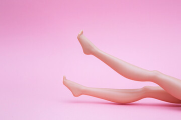 Plastic dolls legs in air against a pink background