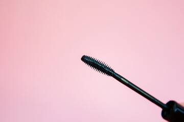 Black mascara wand against a pink peach background 