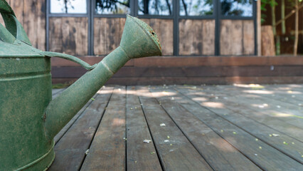 The part of green metal watering can or water sprinkle with wooden wall and wooden floor background