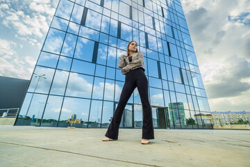 young girl with sunglasses in jacket posing near modern office building with mirrored walls in parking lot with road signs