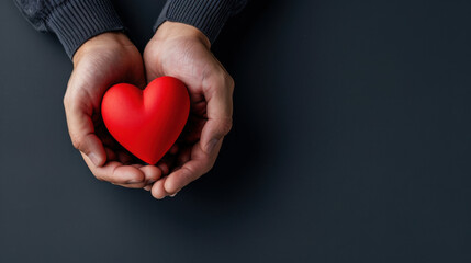 Fototapeta premium Close-up of hands cradling a red heart on a dark background, representing love, protection, and emotional security.