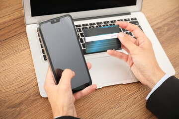 Man with credit card and smartphone at wooden table, closeup