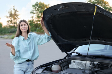 Stressed woman standing near broken car outdoors