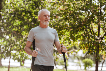 Senior, gray haired man nordic walking in park exercising outdoors for good health