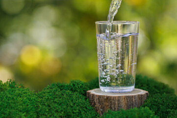 water pouring into glass on stump with moss