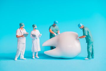 Naklejka premium Miniature Dentists Working on Large Tooth Against Blue Background
