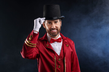 Portrait of showman in red costume and hat on black background with smoke