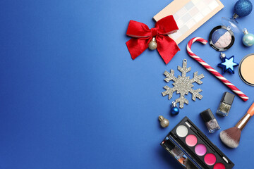 Flat lay composition with makeup products and Christmas decor on blue background. Space for text