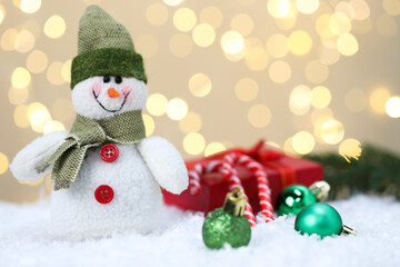 Funny snowman figure, Christmas balls, gift box and candy canes on artificial snow against blurred...