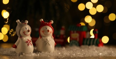 Cute decorative snowmen on artificial snow against blurred lights. Space for text