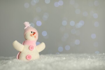 Cute decorative snowman on artificial snow against blurred lights. Space for text
