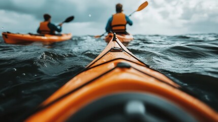 Two kayakers dressed in orange life jackets seen paddling through the challenging and rough ocean waters under a cloudy sky, showcasing an adventurous spirit.