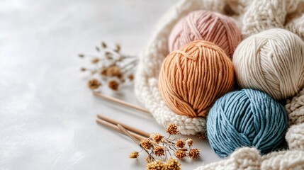 Colorful yarn balls are sitting on white knitted fabric with wooden knitting needles and dried flowers