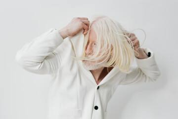 White fashion, modern aesthetics A man with long white hair pulls a hoodie over his head against a clean, light background Stylish and contemporary vibe