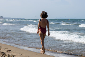 Elderly Woman in Red One-Piece Swimsuit Enjoying a Walk on the Sandy Beach by the Sea
