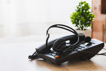 A black phone with a headset on it sits on a desk