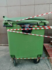  Green trash can tied with ribbon.  Green trash can on the street. Green trash can on wheels.