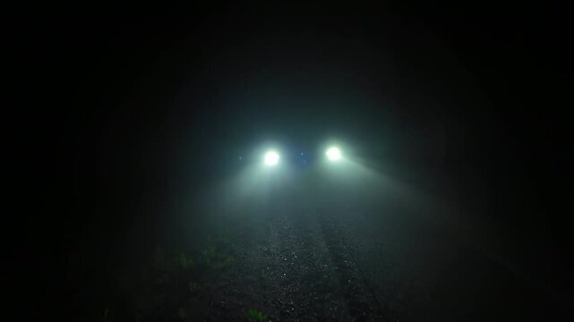 Vehicle front lights showing sparkling severe heavy fog particles randomly spin in the air. Smoky and foggy night at the pitch dark road. Black background with car light rays and beams.
