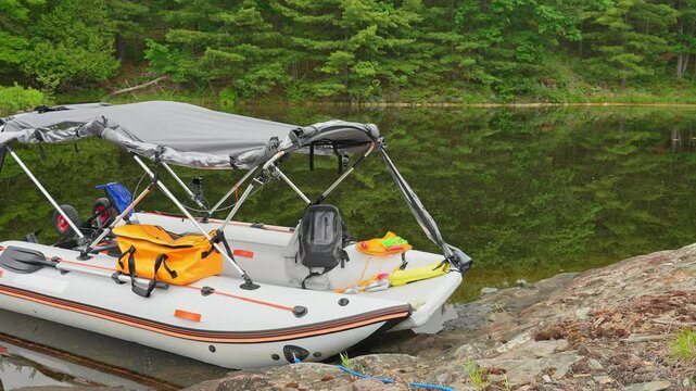 Lonely moored fishing trolling boat floating and drifting at lake bank at wilderness lake. Anchored to small island empty boat. Inflatable motorized boat with tent swaying on tranquil water at morning