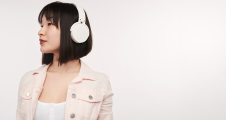 Young woman enjoying music with white headphones, dressed casually in a light jacket, looking relaxed and thoughtful.