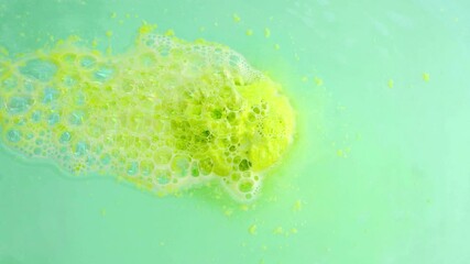 The green bath bomb dissolves in the bath water, close up
