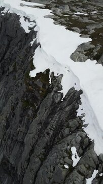 Aerial view of a rocky mountain top with snow in the crevices and patches of green vegetation. British Columbia, Canada.