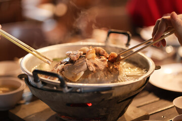 Grill pork using chopsticks on a pan and smoke rises above. Grilling is a popular food among Asians.