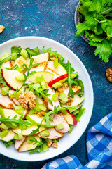 Foodie food salad with crispy apple, celery, lettuce, griled chicken slices, arugula and walnuts on blue background, top view