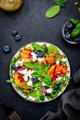 Foodie food salad with grilled peaches, blueberries, red onion, feta cheese, basil and arugula on black background, top view