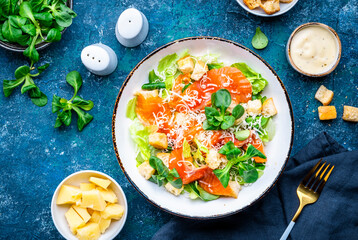Foodie food caesar salad with salmon, iceberg  lettuce, croutons, grated parmesan with dressing. Blue background, top view