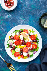 Greek salad with feta cheese, olives, tomatoes, lettuce, paprika, cucumber and onion. Blue background, top view