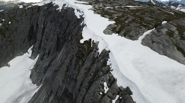 Aerial view of a steep, rocky mountain top with patches of snow, showcasing the rugged beauty and stark contrast of nature. British Columbia, Canada.