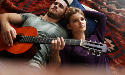 Obraz premium Couple, relax and guitar in home for bonding, love and music together on floor with blanket or pillow. Man, woman and playing instrument in apartment for romance, relationship or comfort with support