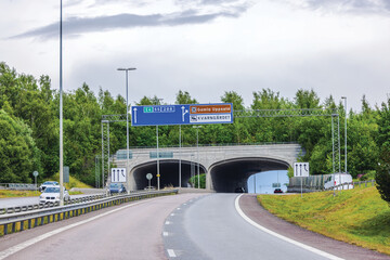 Highway entrance to tunnel near Uppsala with road signs and trees in Sweden.