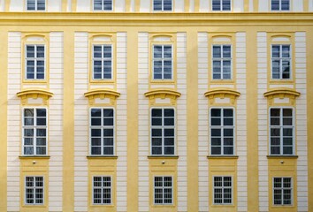 The historic European building facade features ornate yellow walls with barred windows and...