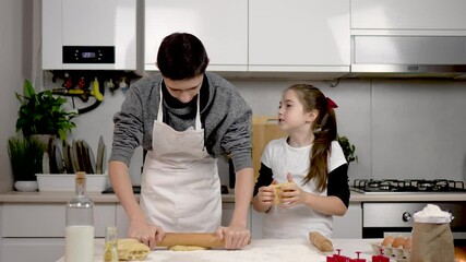 Lovely brother and sister cooking cookies at kitchen together. Boy rolls dough with rolling pin on table. Girl forms cake in hands. Family preparing at home. Teenage children making dough for holiday - Powered by Adobe